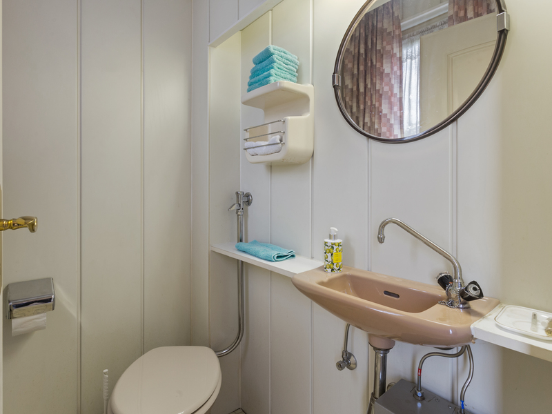 Kleines Badezimmer mit rosafarbenem Waschbecken, WC, Regal mit Handtüchern und rundem Spiegel.