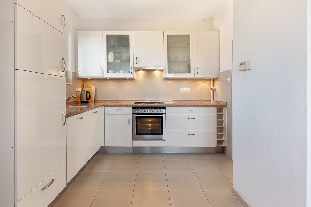 Moderne Einbauküche mit weißen Schränken, Backofen, Herd und Kaffeemaschine.
