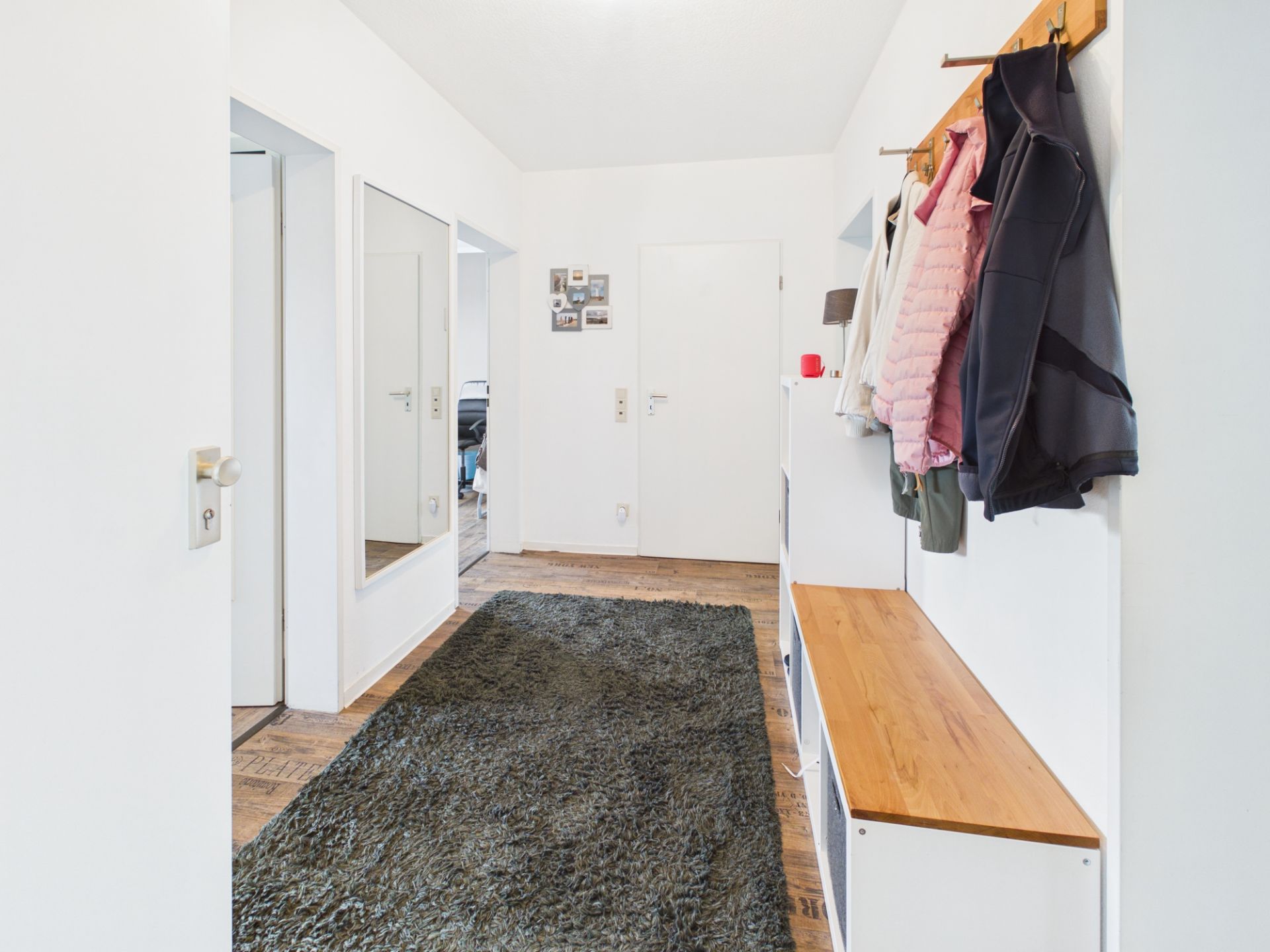 Heller Flur mit Spiegel, Garderobe, Sitzbank und Teppich auf Holzfußboden.