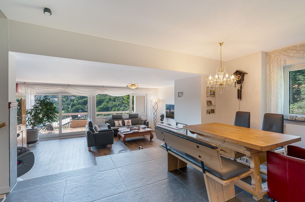 Modernes Wohnzimmer mit Essbereich, großen Fenstern und Blick ins Grüne.
