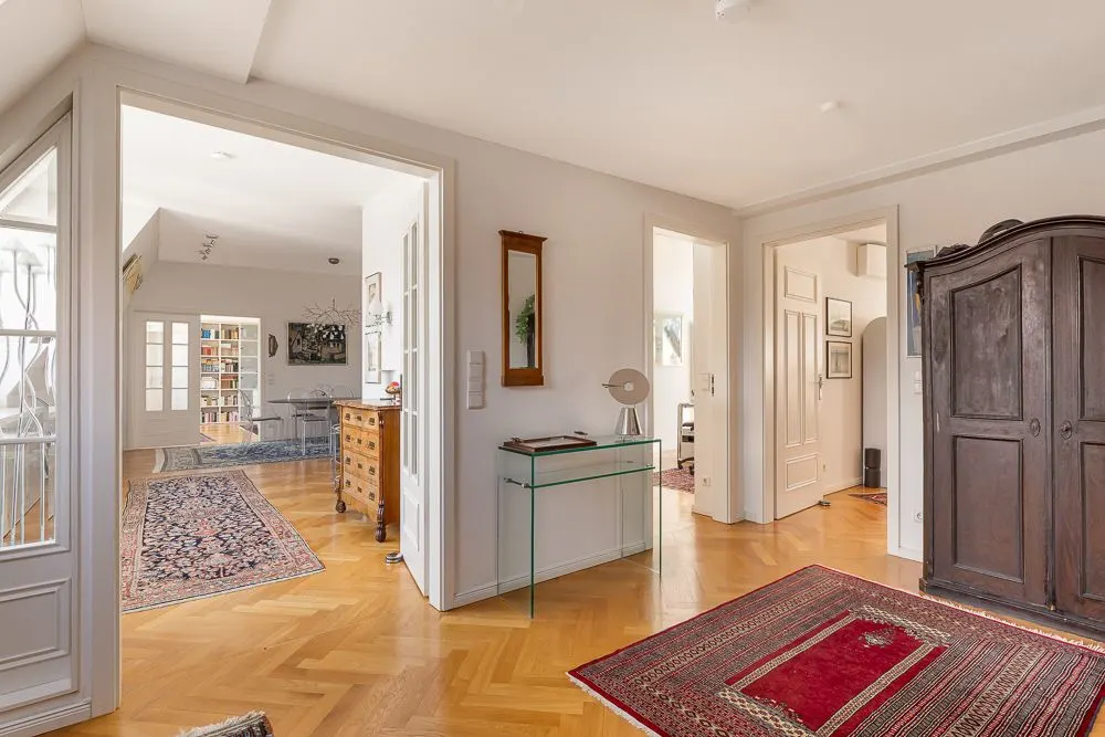 Heller Flur mit Holzboden, Teppichen, Glas-Konsole und Blick in mehrere angrenzende Zimmer.