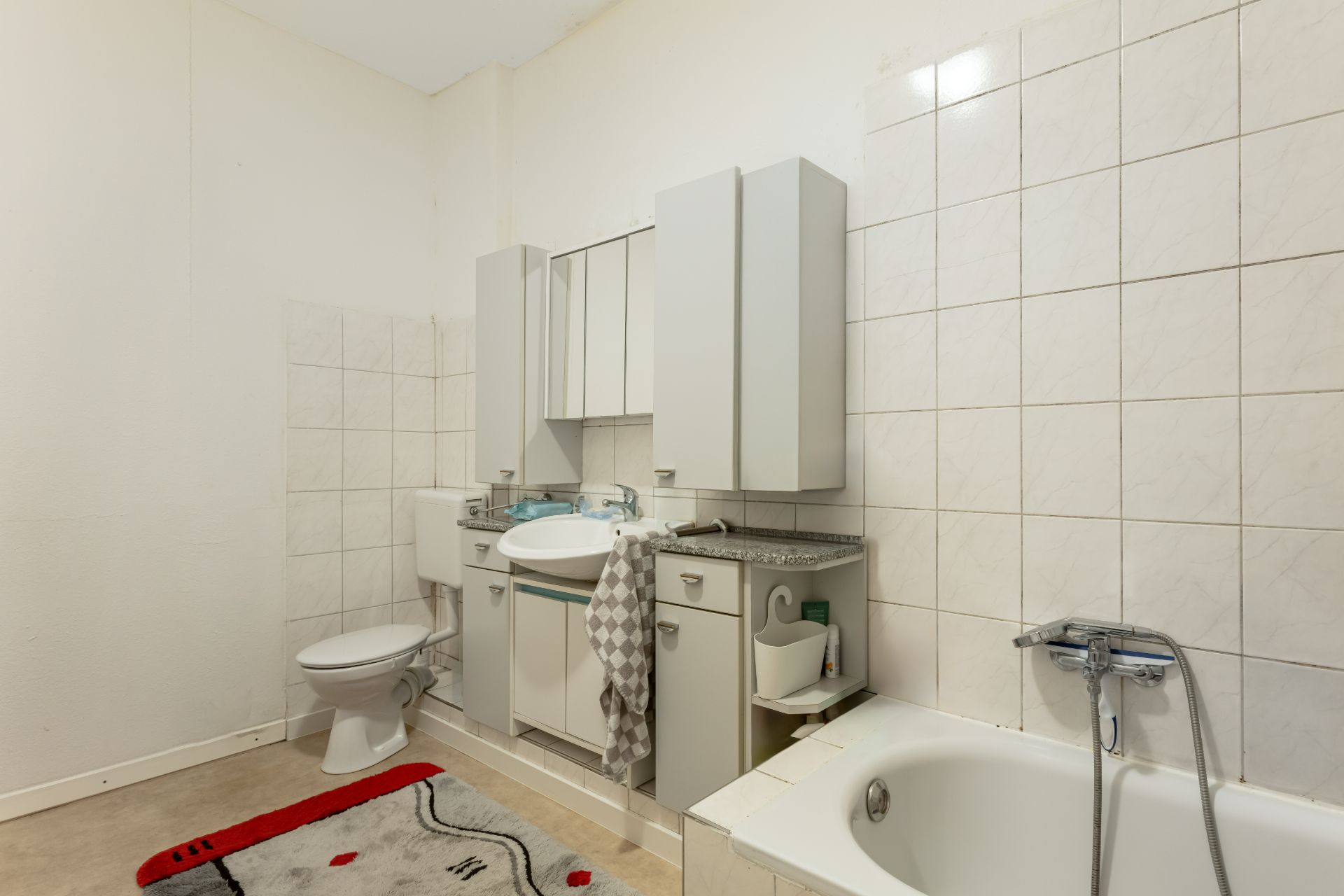 Badezimmer mit Badewanne, Waschbecken, Toilette und Schränken, Fliesen an den Wänden.
