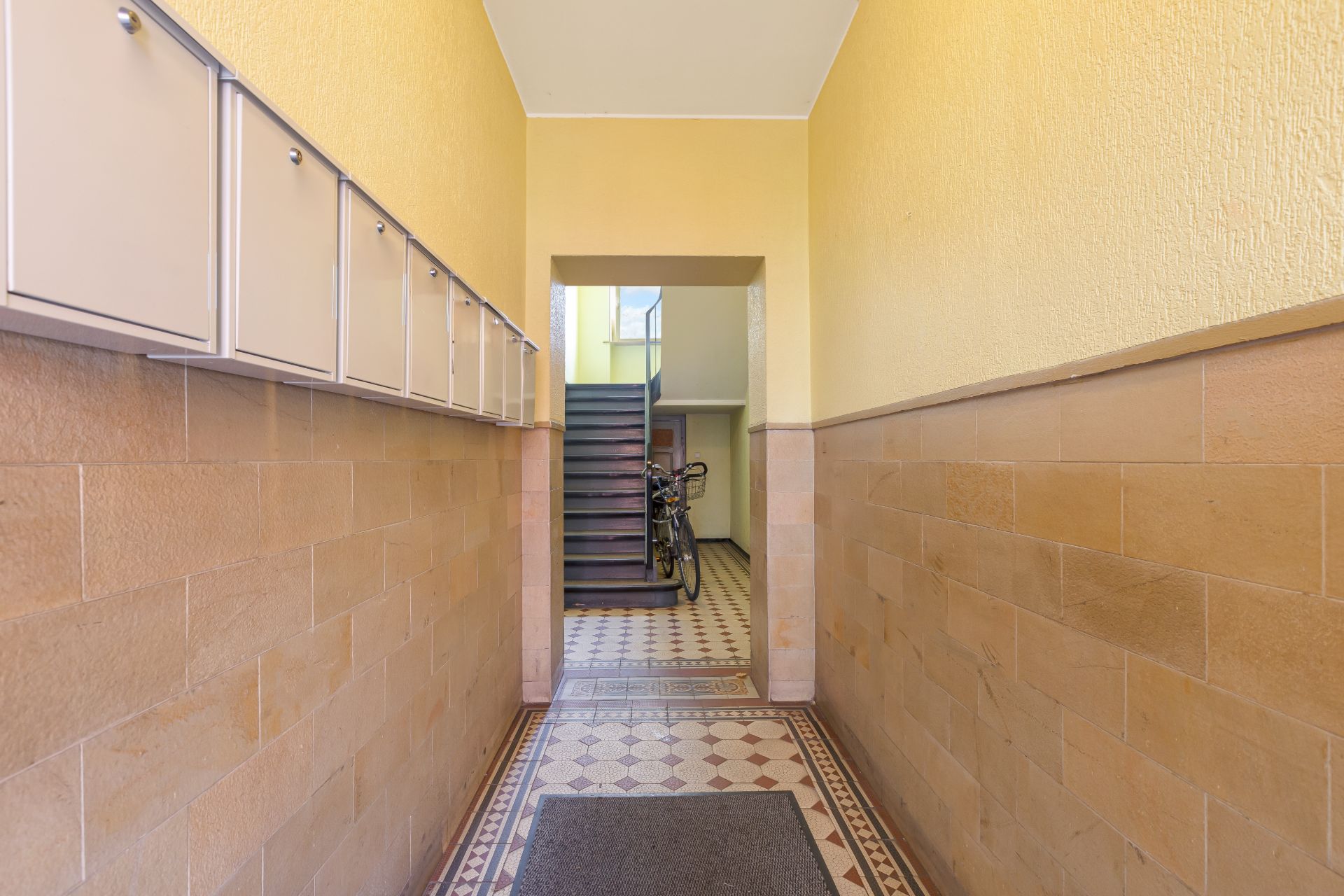 Hausflur mit Briefkästen an der Wand, Fliesenboden und Treppe im Hintergrund.