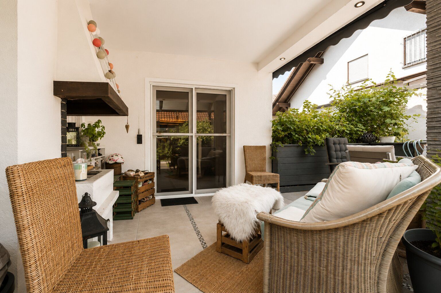 Überdachte Terrasse mit Sitzmöbeln, Holztisch, Pflanzen und Schiebetür zum Haus.