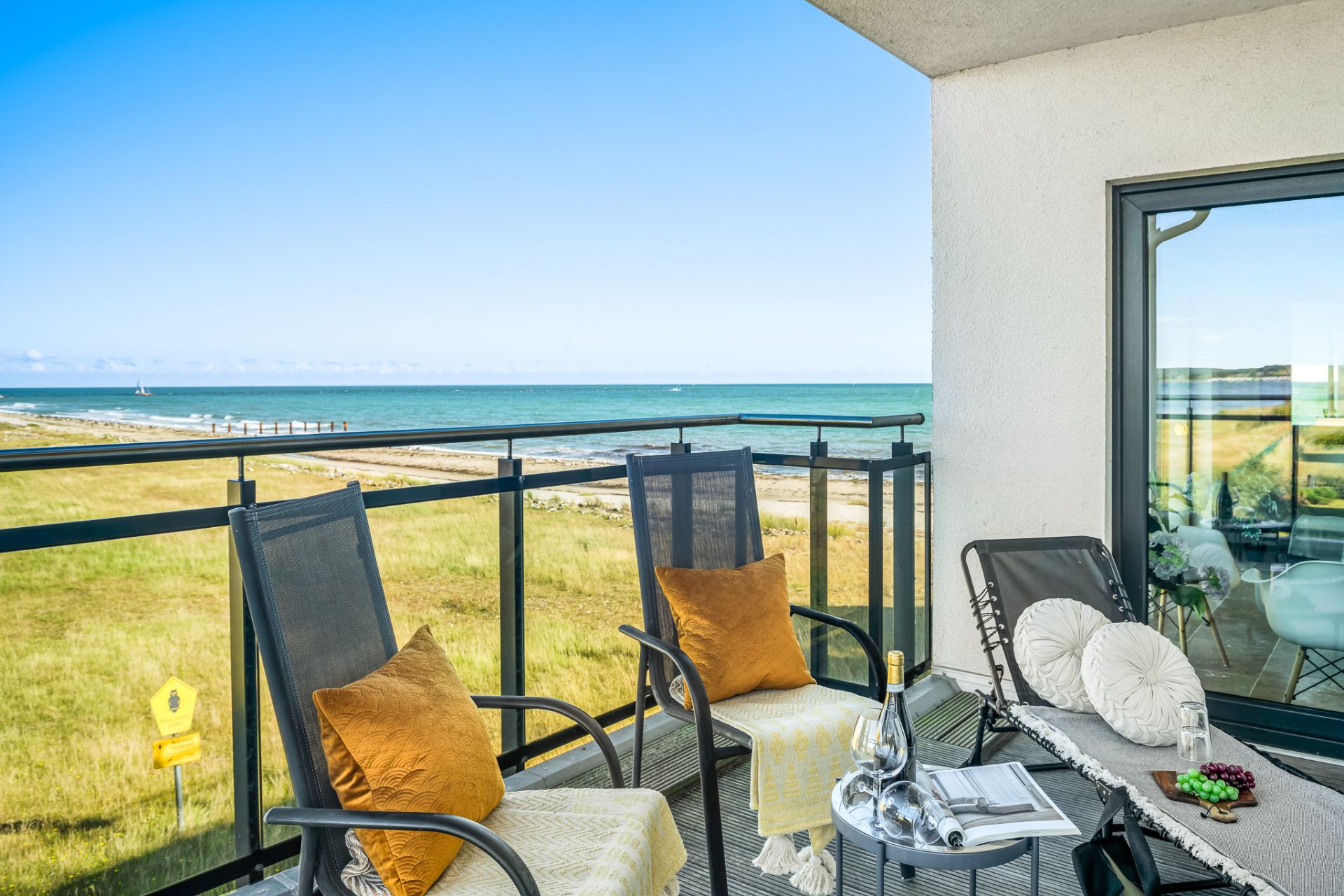 Balkon mit zwei Stühlen, Tisch, Kissen und Blick auf das Meer und einen Sandstrand.