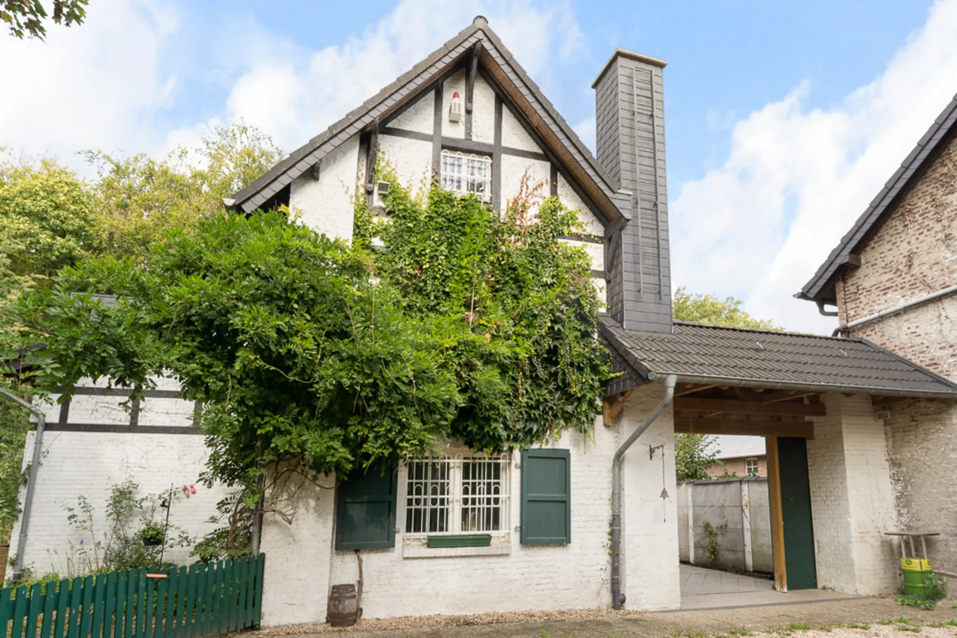Weißes Fachwerkhaus mit grün bewachsener Fassade und grünen Fensterläden.