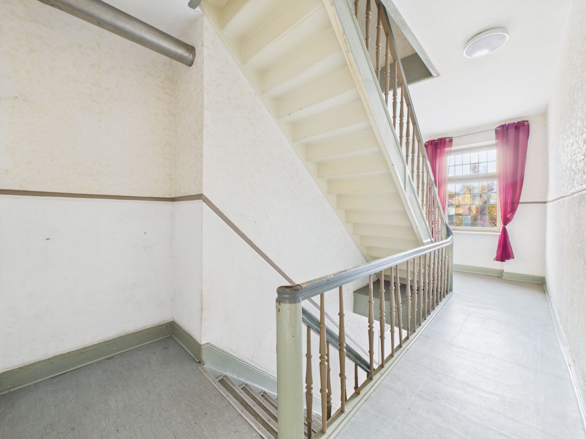 Helles Treppenhaus mit weißer Treppe, Fenster und roten Vorhängen.
