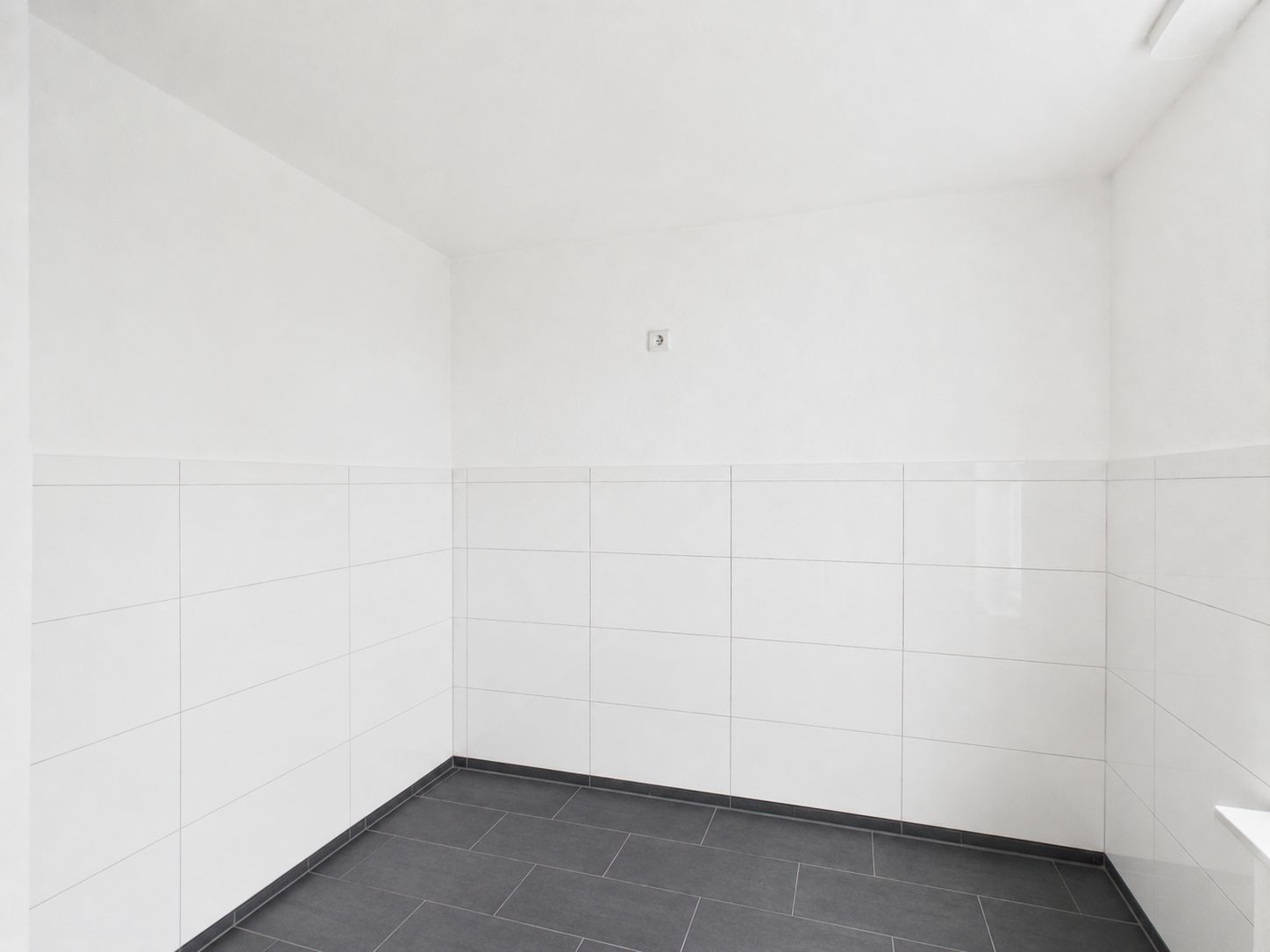Leerer Raum mit weißen Wandfliesen und dunklem Bodenfliesen.