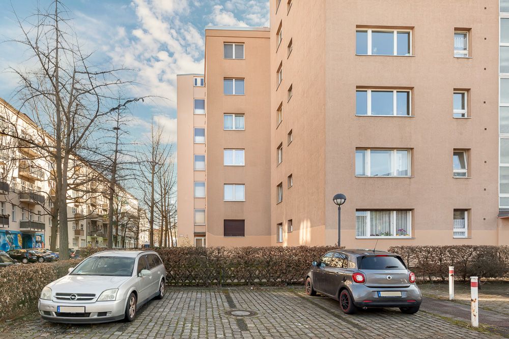 Zwei Autos parken vor einem mehrstöckigen Wohnhaus mit mehreren Fenstern und umliegenden Büschen.