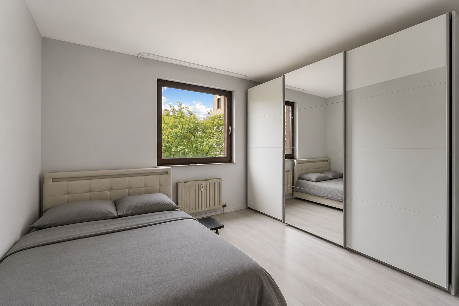 Schlafzimmer mit Doppelbett, großem Spiegel-Kleiderschrank und Fenster mit Blick ins Grüne.