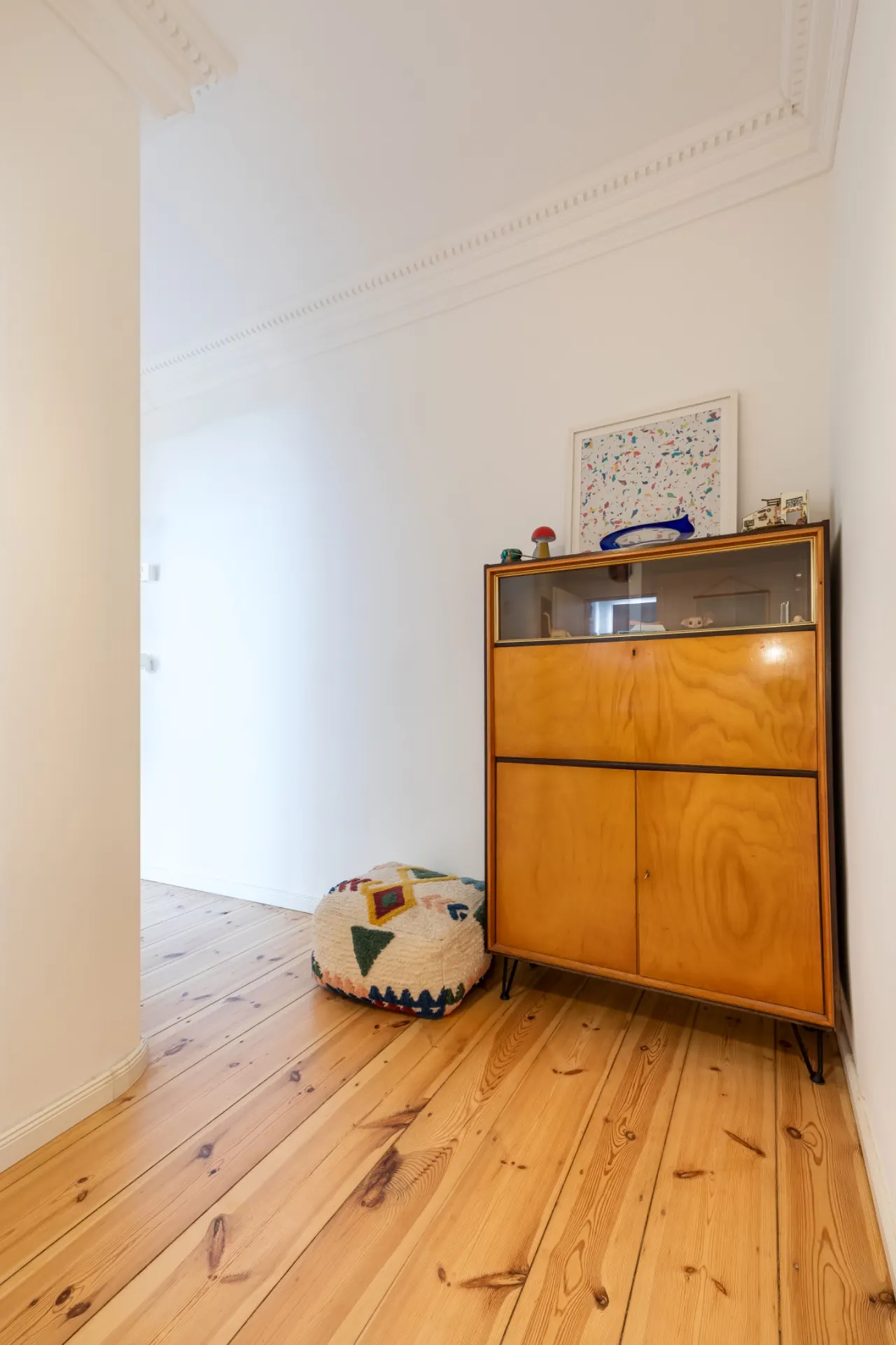 Heller Flur mit Holzschrank, Hocker mit Muster und gerahmtem Bild an der Wand.
