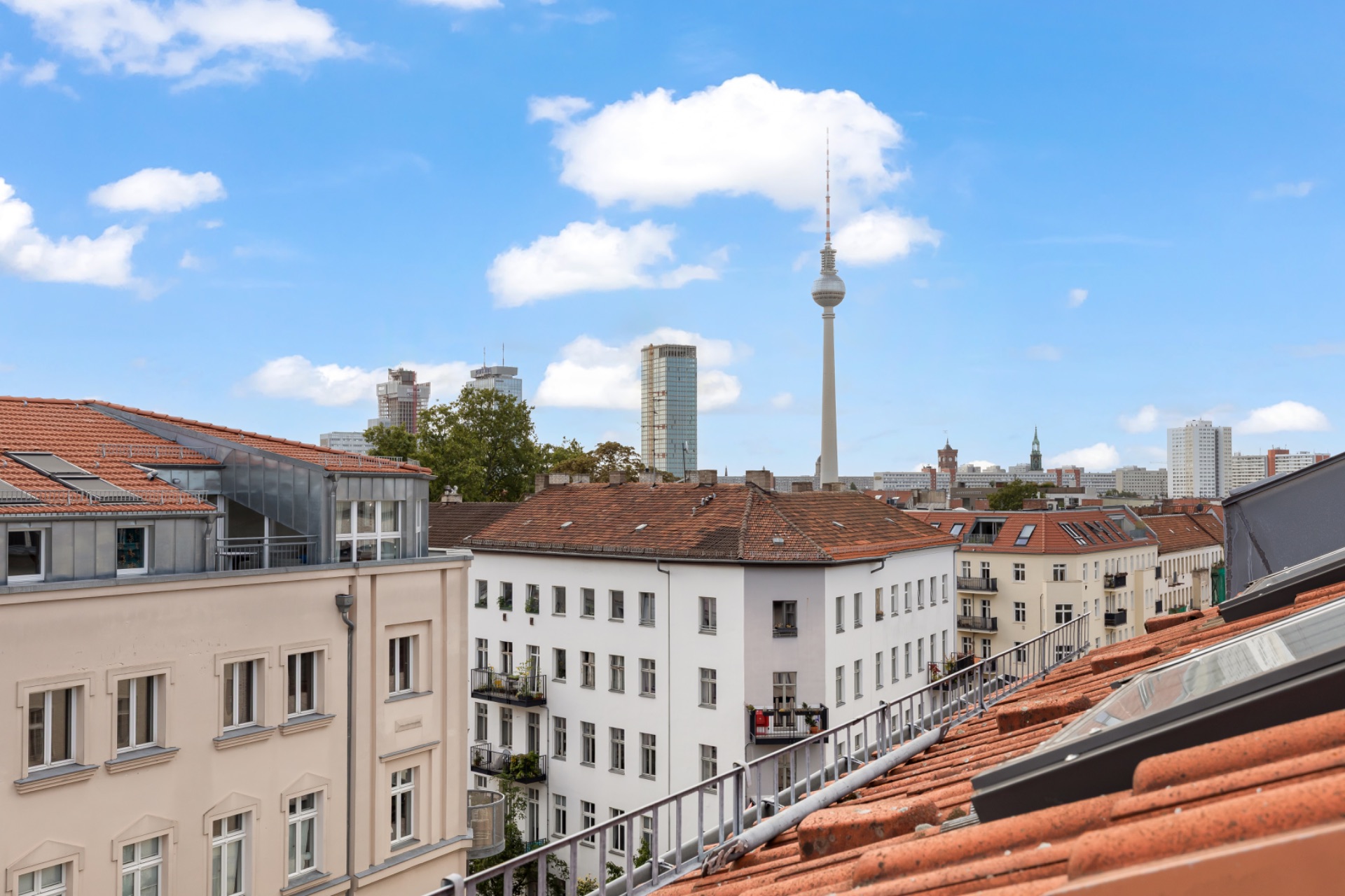Blick über Berliner Wohnhäuser mit Fernsehturm im Hintergrund und blauem Himmel.