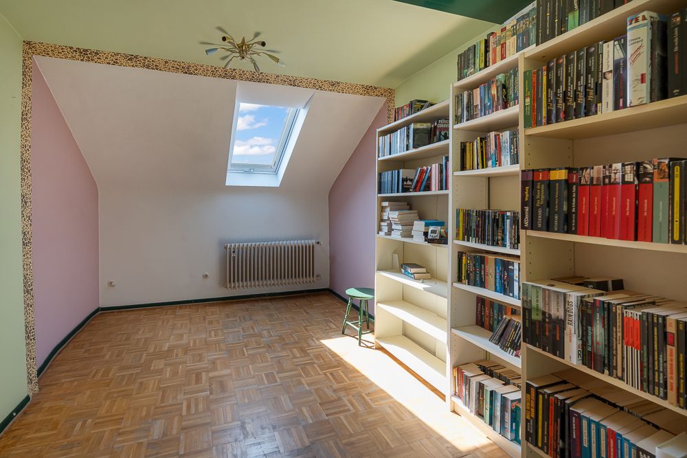 Heller Raum mit Bücherregalen, Parkettboden, Dachfenster und Heizkörper an der Wand.