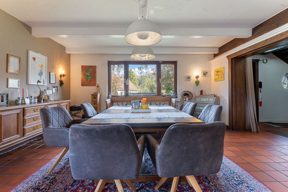 Esszimmer mit großem Holztisch, sechs Stühlen, Teppich und großen Fenstern im Hintergrund.