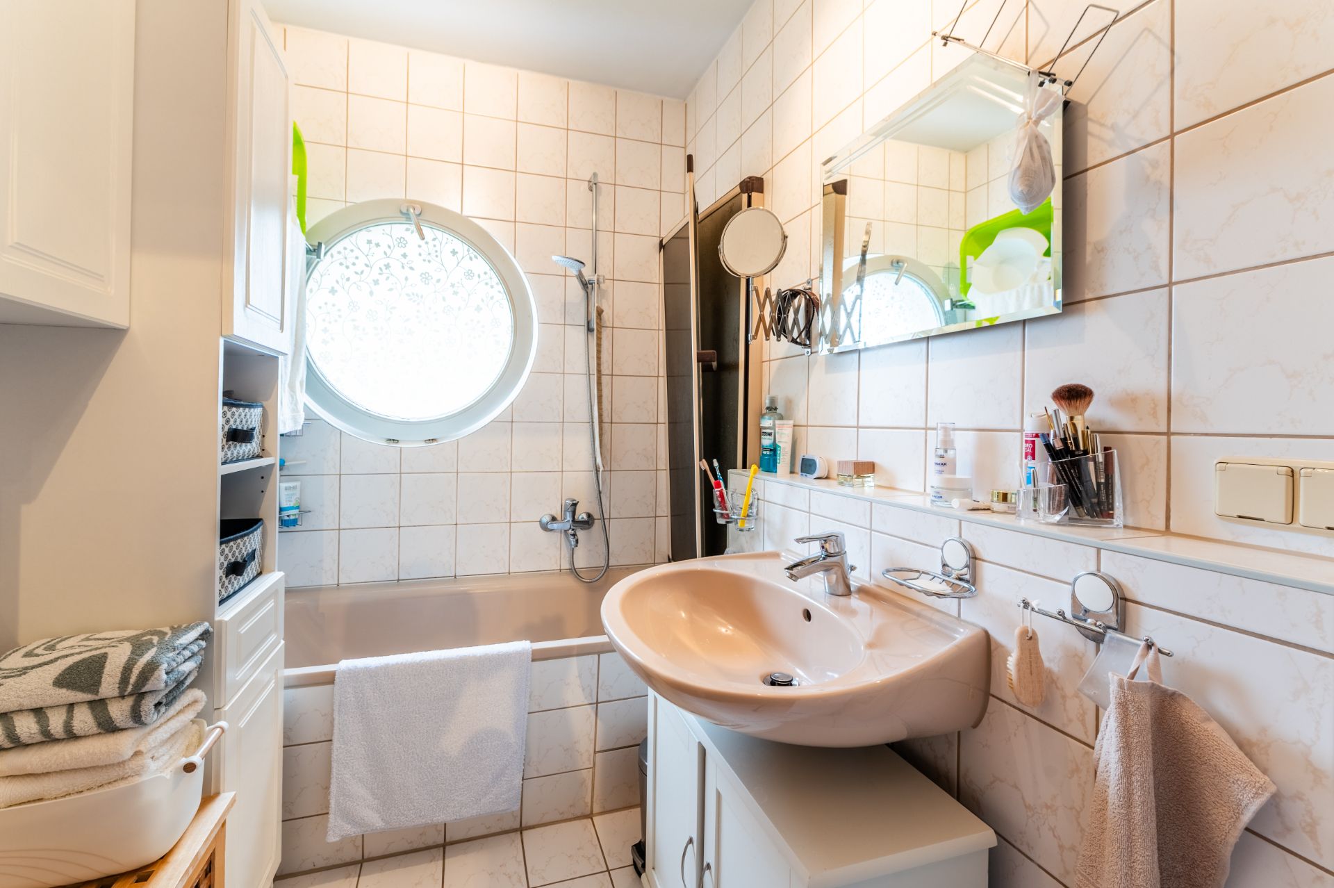 Helles Badezimmer mit runder Fenster, Badewanne, Waschbecken und weißen Fliesen.