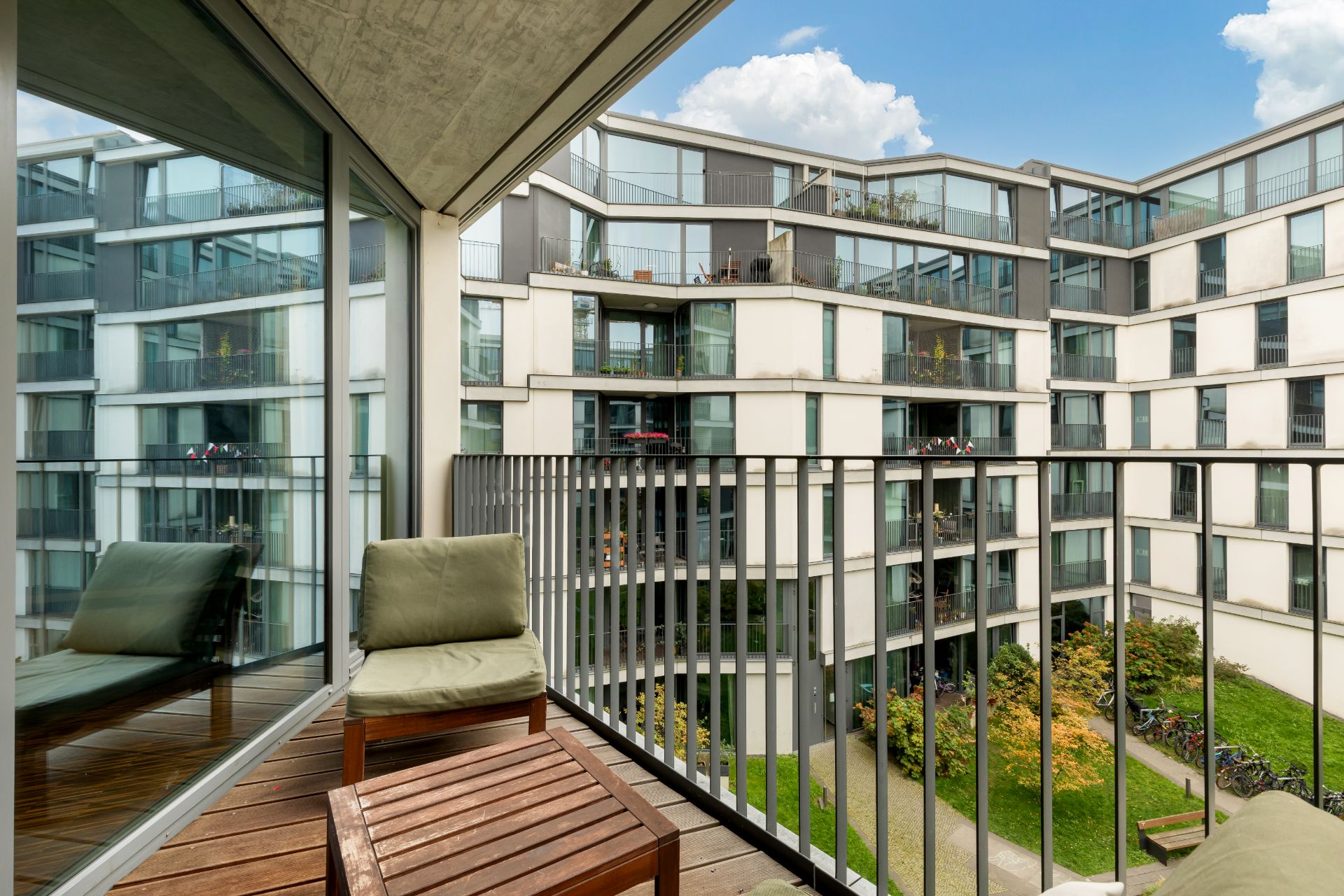 Balkon mit Stuhl und Tisch, Blick auf modernen Innenhof und benachbarte Wohngebäude.