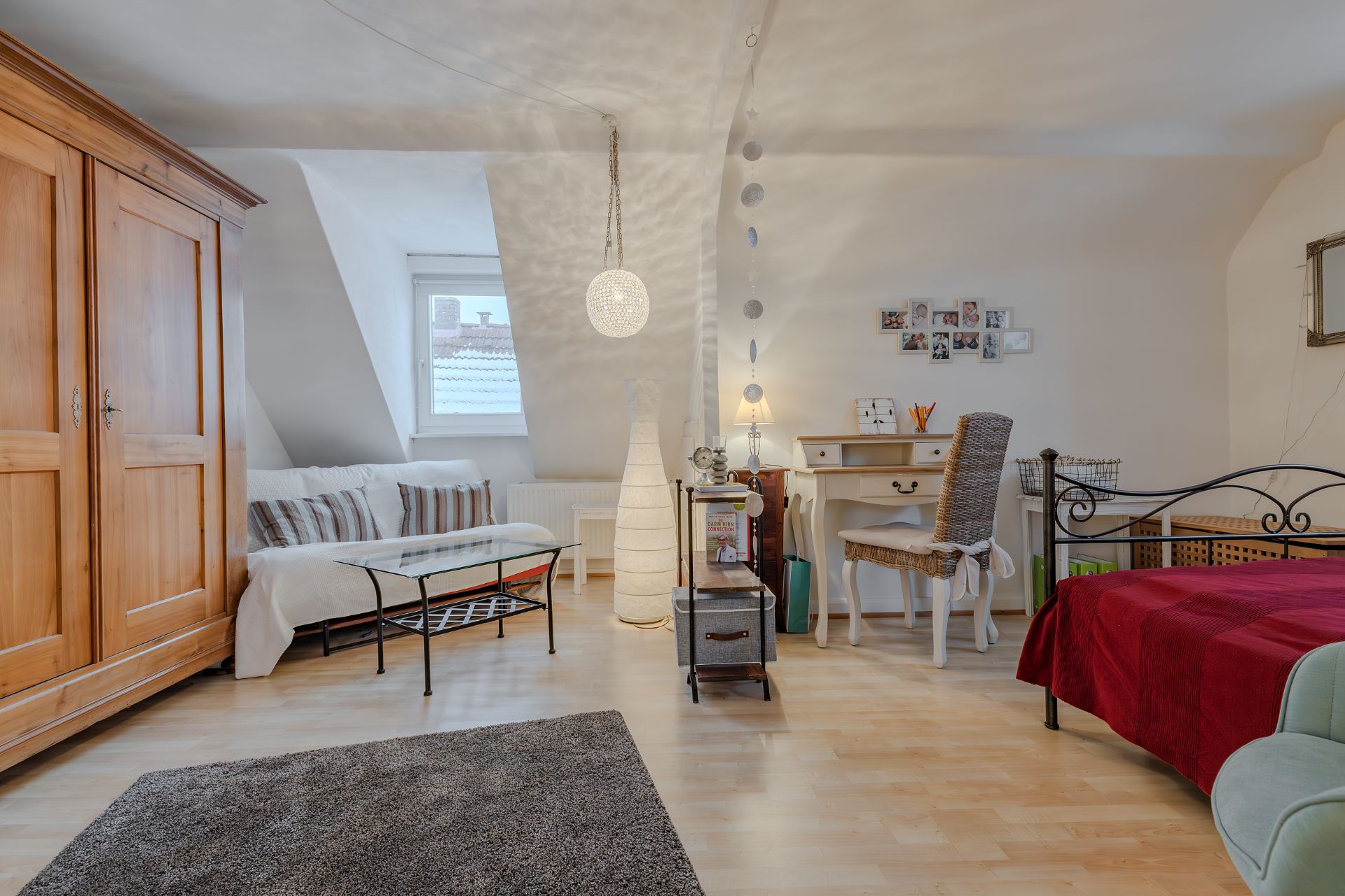 Gemütliches Zimmer mit Sofa, Schreibtisch, Bett, Kleiderschrank und Fenster.