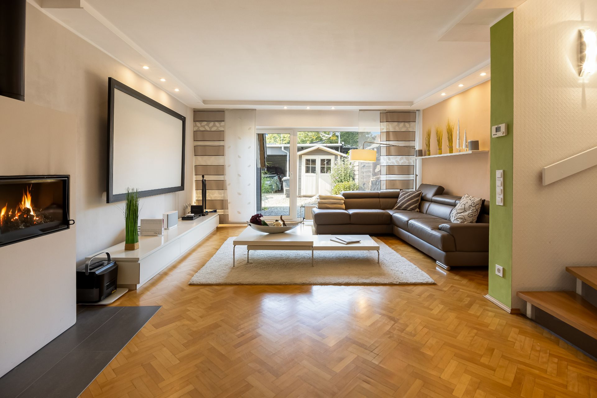 Helles Wohnzimmer mit Ecksofa, Kamin, Couchtisch und großem Fenster zum Garten.