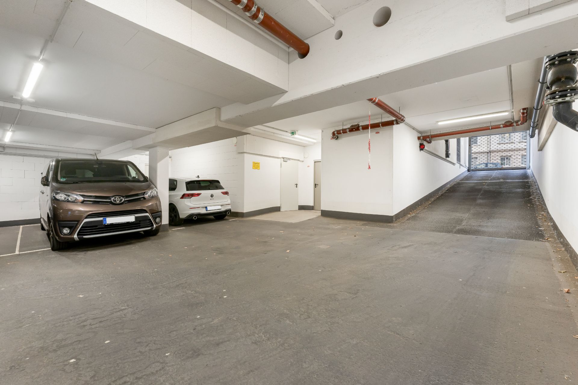 Tiefgarage mit zwei geparkten Autos und Einfahrt nach draußen.