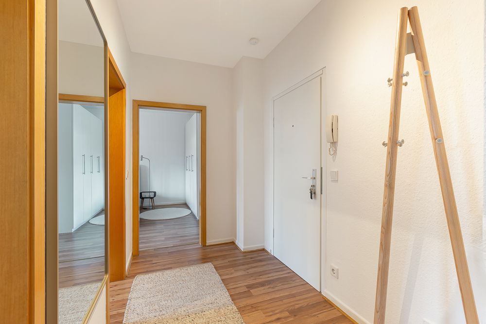 Heller Flur mit Holzfußboden, Spiegel, Teppich und Blick in einen angrenzenden Raum mit Schrank.