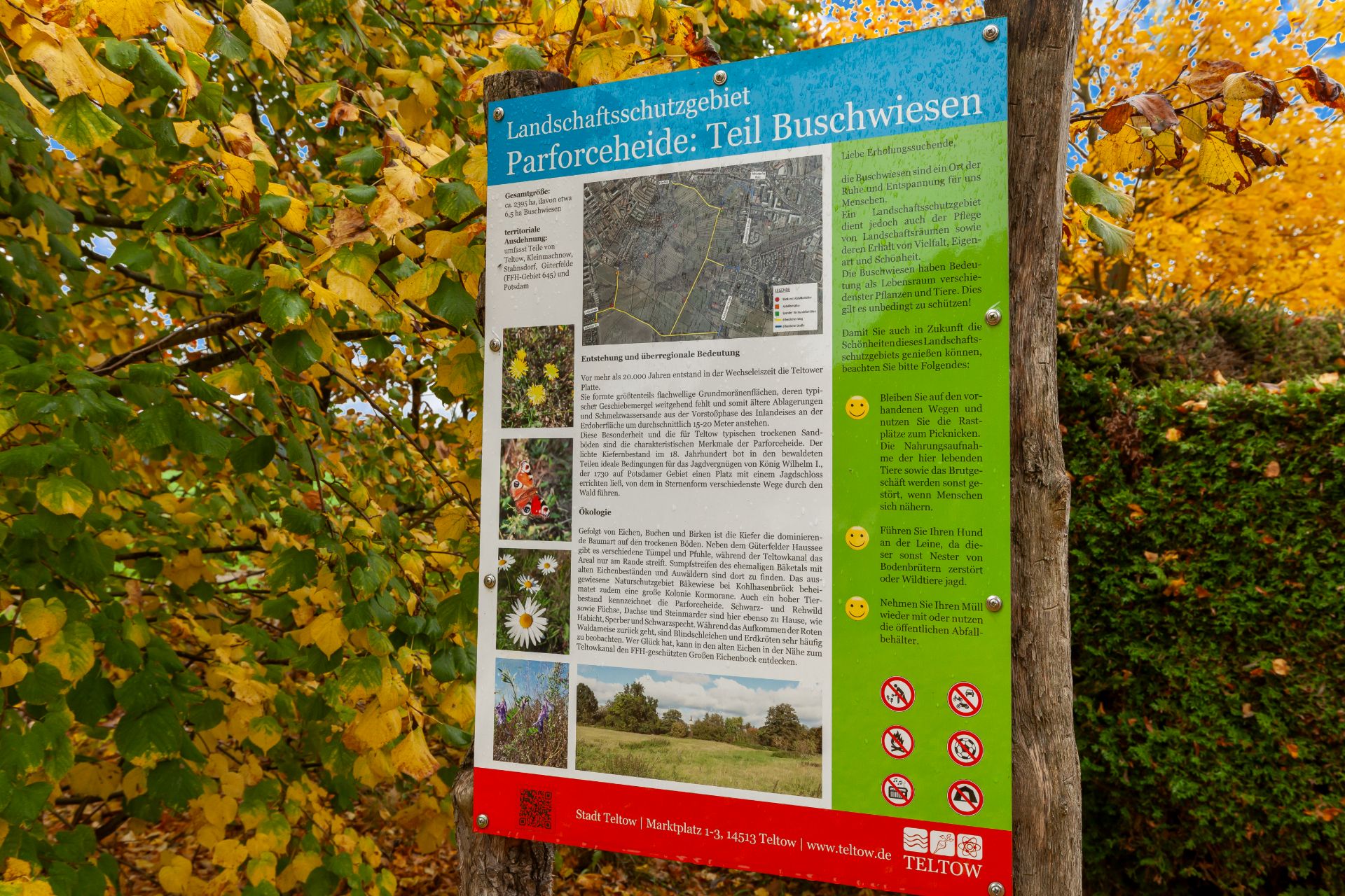 Informationsschild zum Landschaftsschutzgebiet vor herbstlich gefärbten Bäumen.