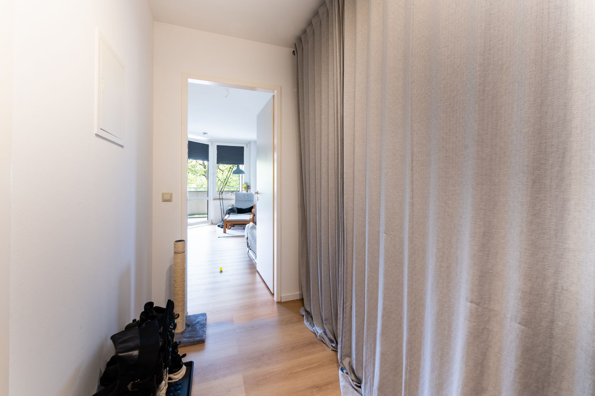 Flur mit Holzfußboden, Garderobe rechts und Blick in ein helles Schlafzimmer.