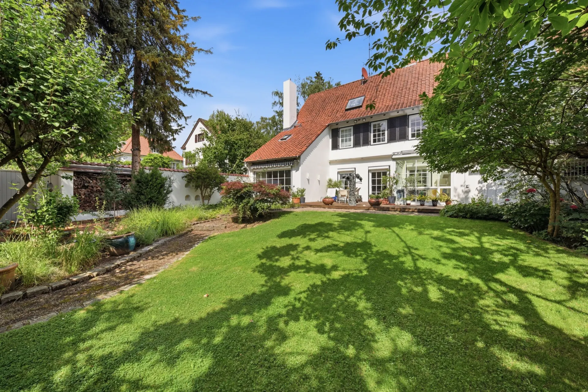 Großer Garten mit Rasenfläche und Bäumen vor einem weißen Wohnhaus mit rotem Dach.