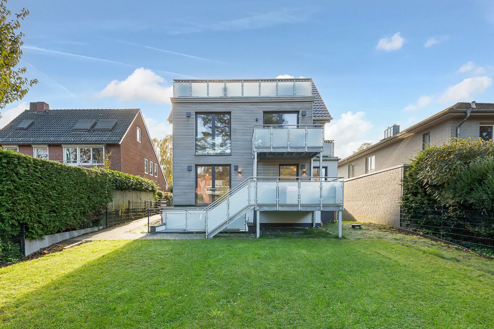 Modernes Wohnhaus mit Balkon und großem Garten, aufgenommen von hinten bei Tageslicht.