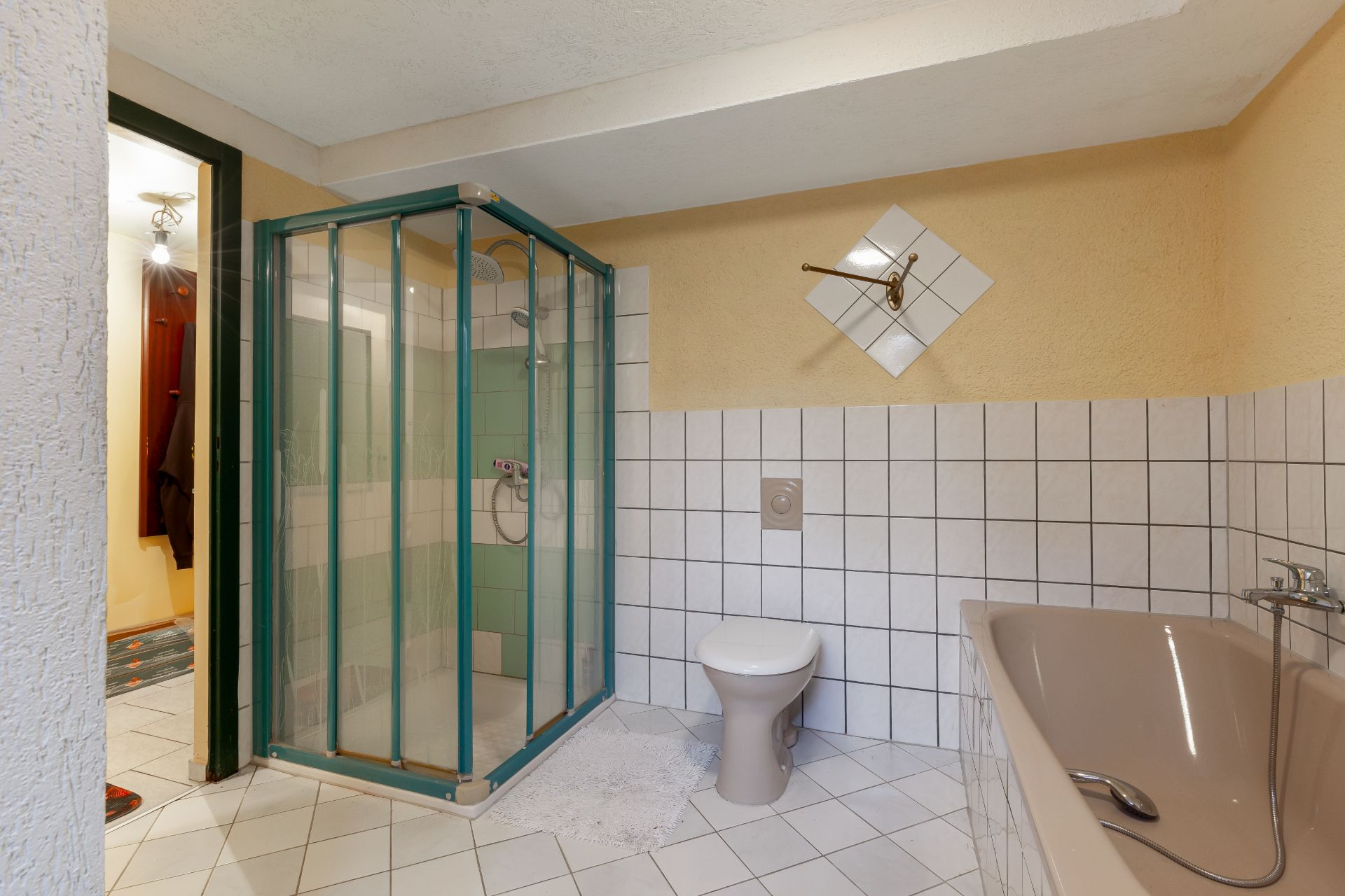 Badezimmer mit Dusche, Toilette und Badewanne, weiße Fliesen an Boden und Wand.