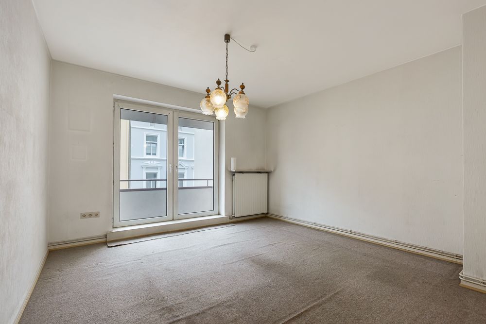 Leeres Zimmer mit Teppichboden, großen Fenstern, Balkon und Deckenleuchte.