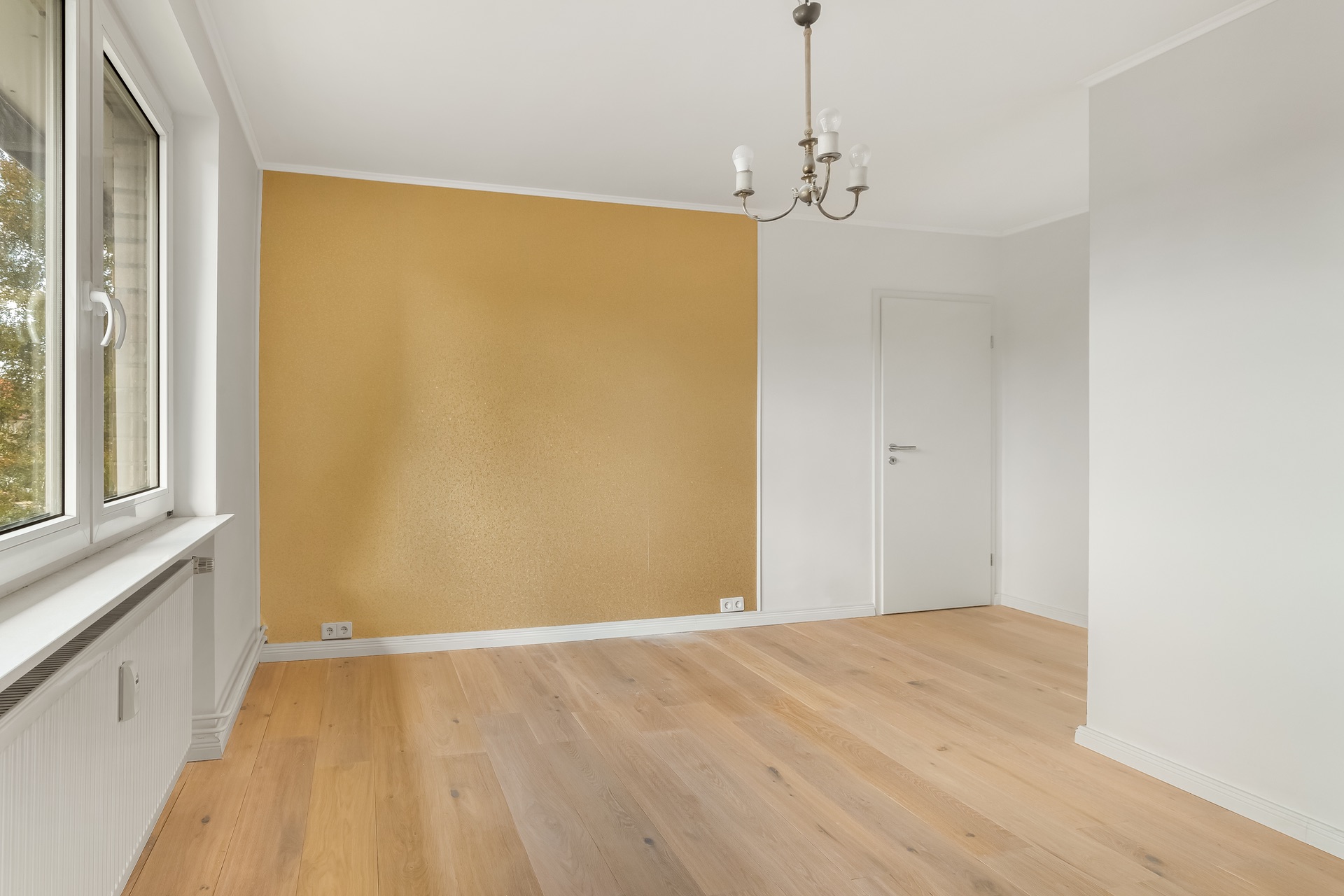 Leerer Raum mit Holzfußboden, gelber Wand, Fenster und Deckenleuchte.