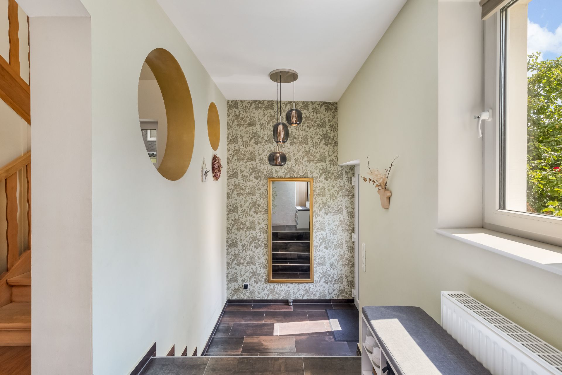 Heller Flur mit gemusterter Tapete, Wandspiegel, runden Wanddekoren und Holztreppe.