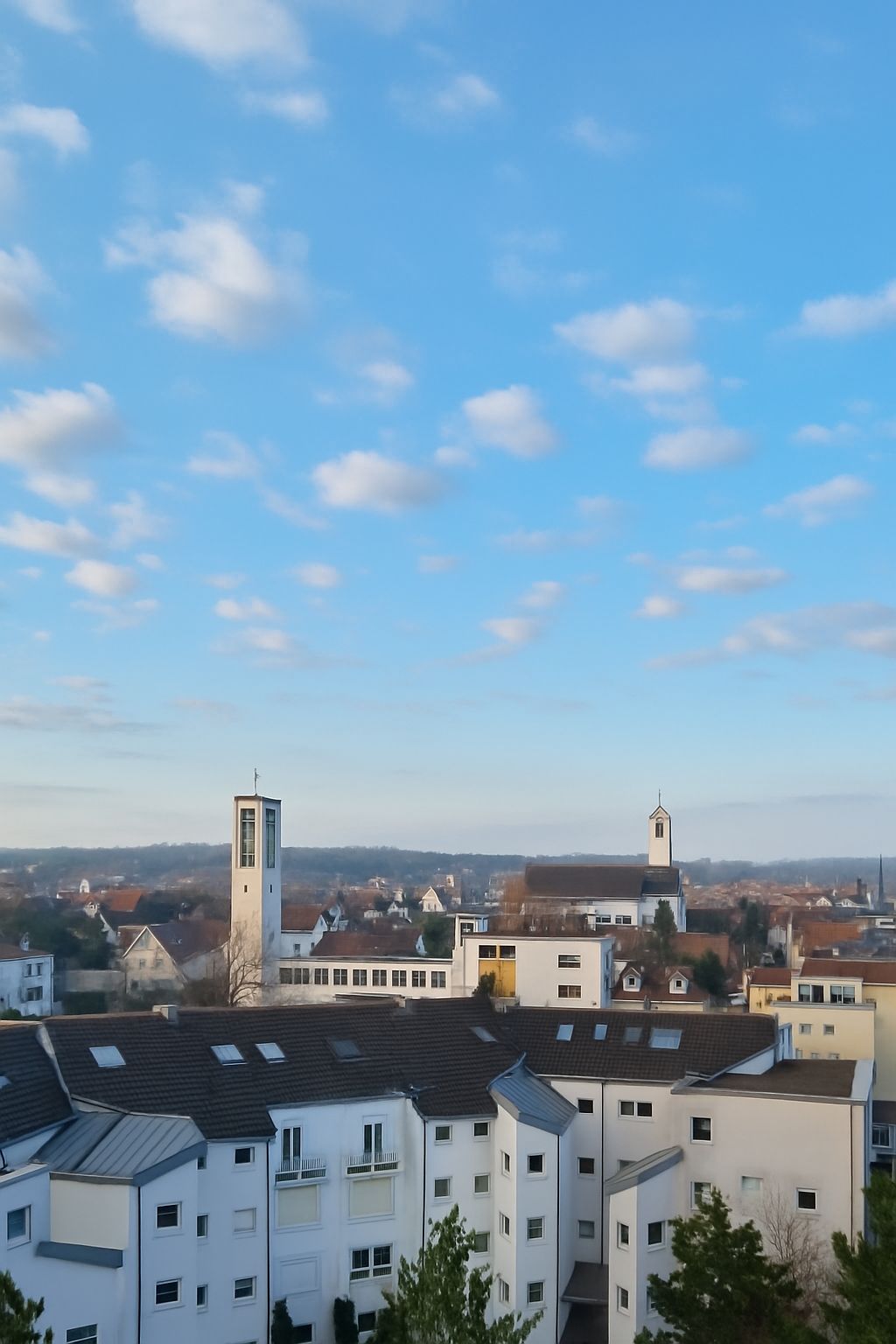 Mehrstöckige Wohnhäuser mit Kirche im Hintergrund unter blauem Himmel mit Wolken.