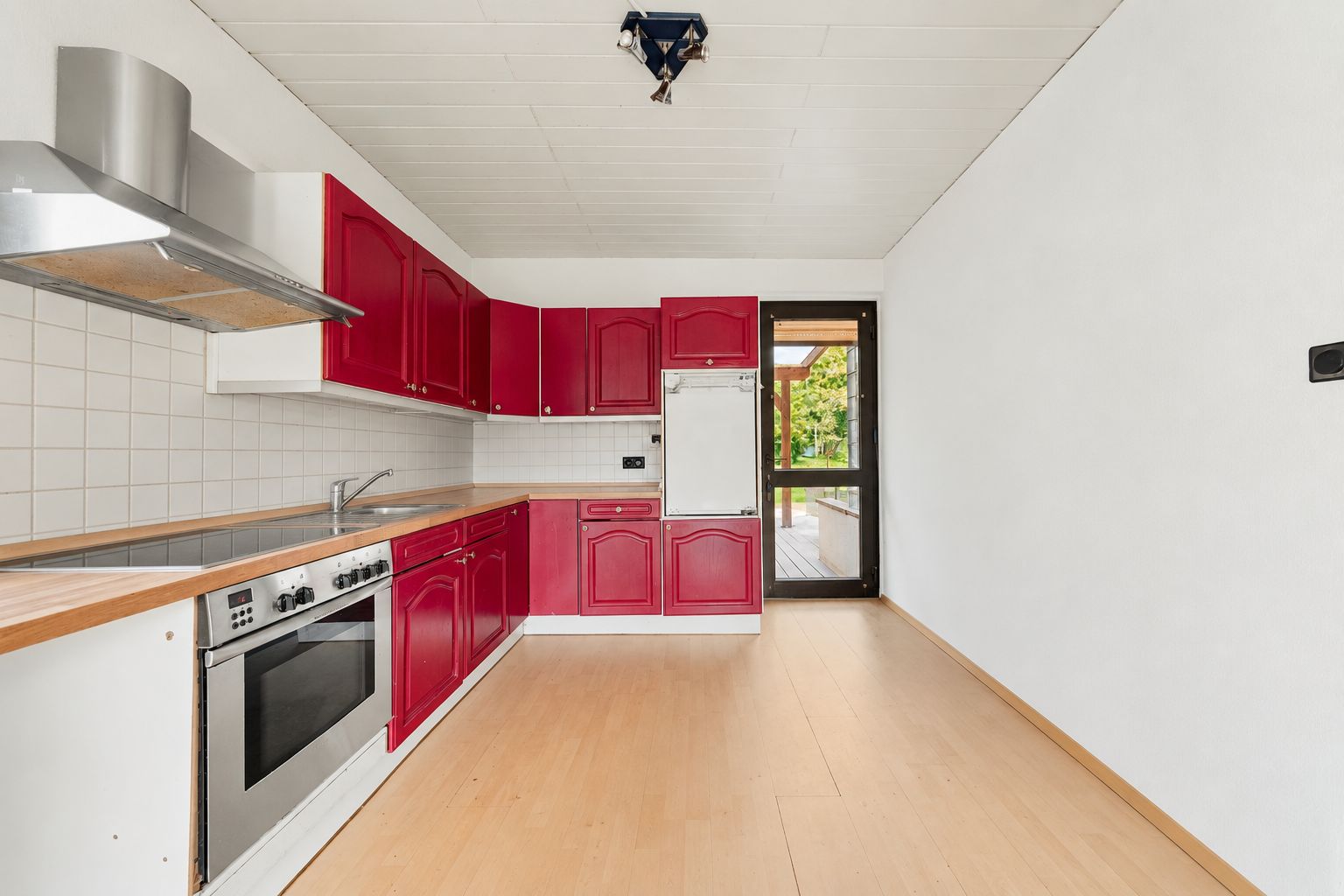 Küche mit roten Schränken, Herd, Spüle und großem Fenster zur Terrasse.