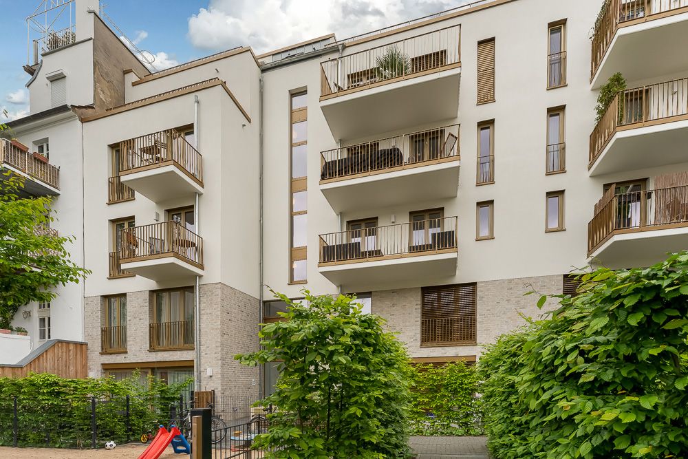 Moderne Wohnhausfassade mit mehreren Balkonen und Grünpflanzen davor.