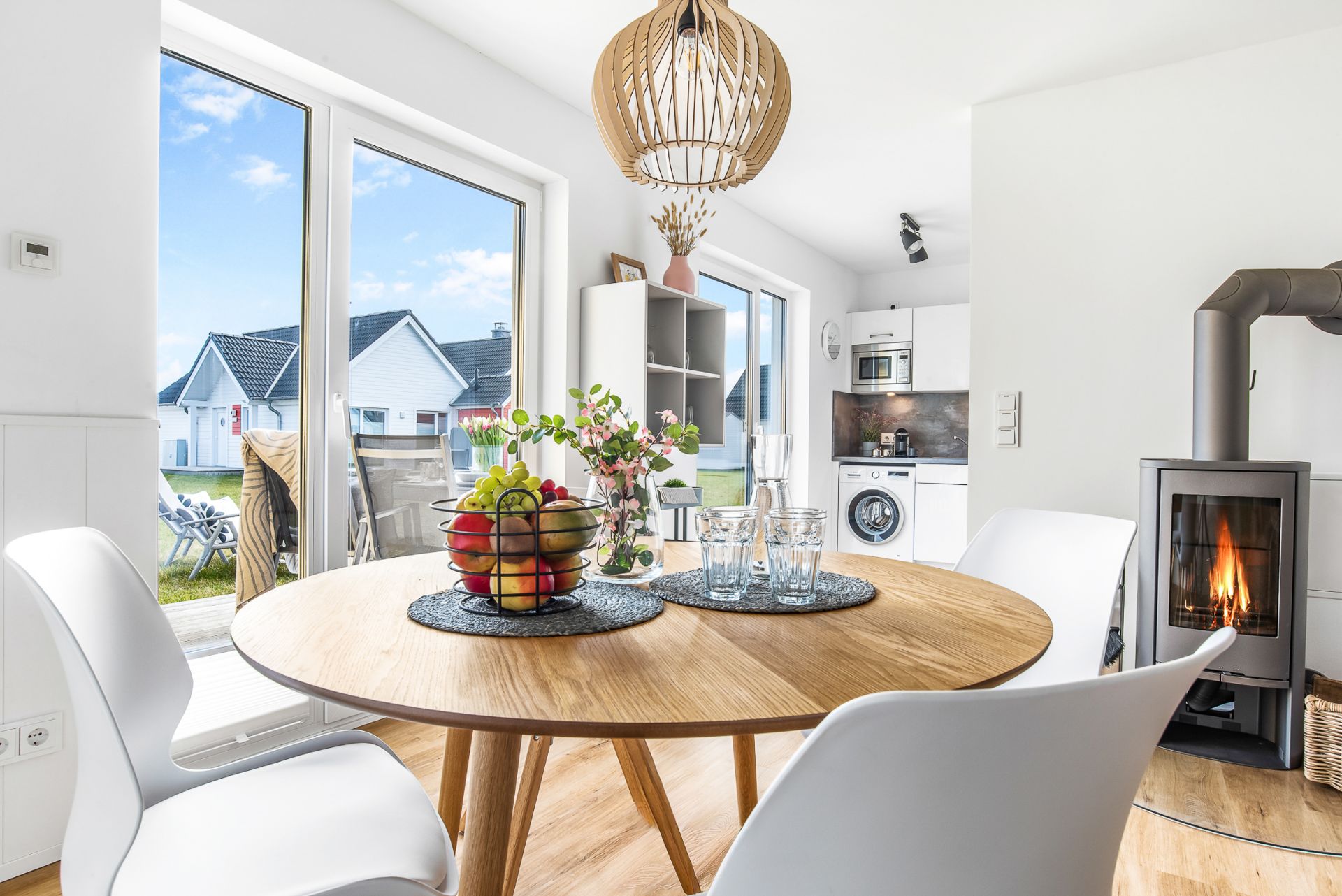 Heller Essbereich mit rundem Holztisch, Kaminofen und Blick in eine moderne Küche.