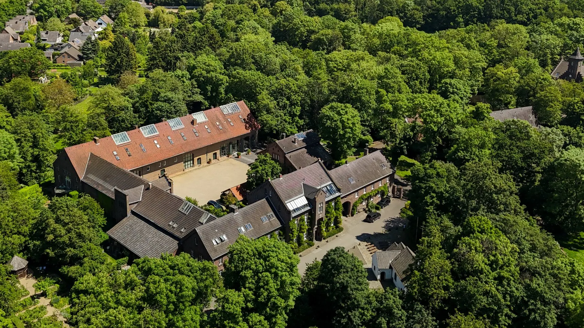 Luftaufnahme eines großen Wohngebäudekomplexes mit Innenhof, umgeben von Bäumen.