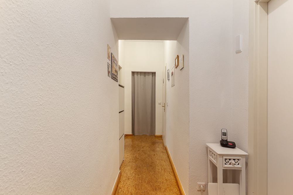 Heller Flur mit Holzfußboden, weißen Wänden und einem kleinen weißen Tisch mit Telefon.
