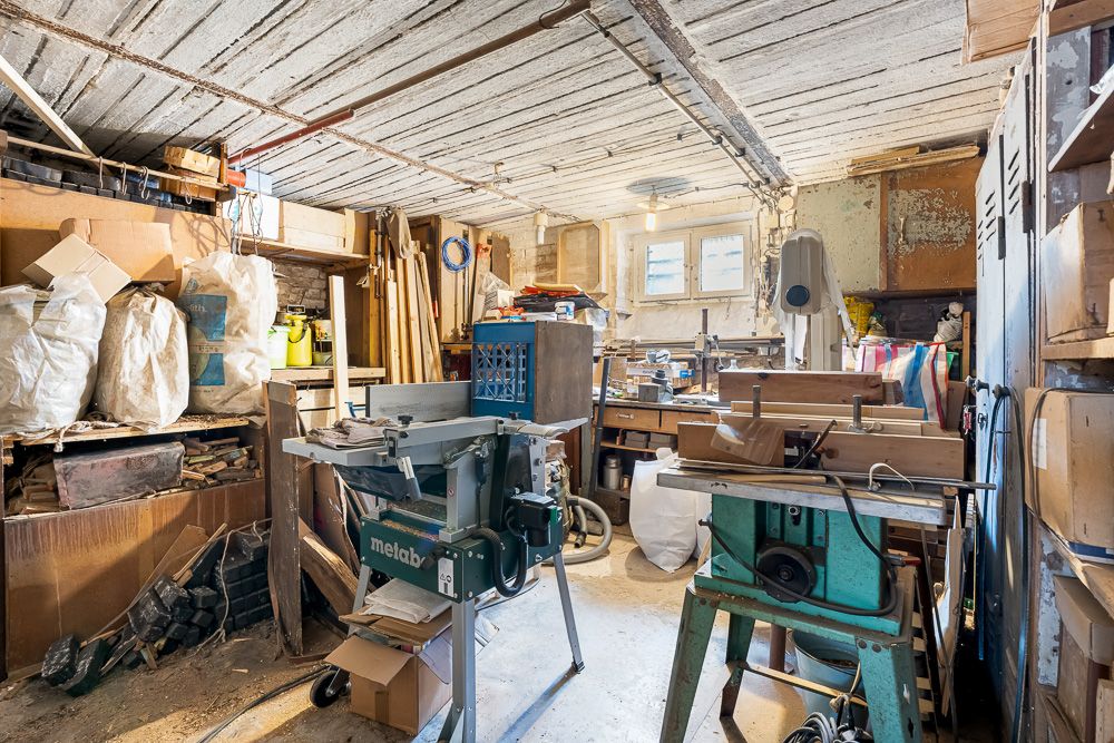 Werkstattraum mit Holzbearbeitungsmaschinen, Werkbänken und Regalen voller Materialien und Werkzeug.