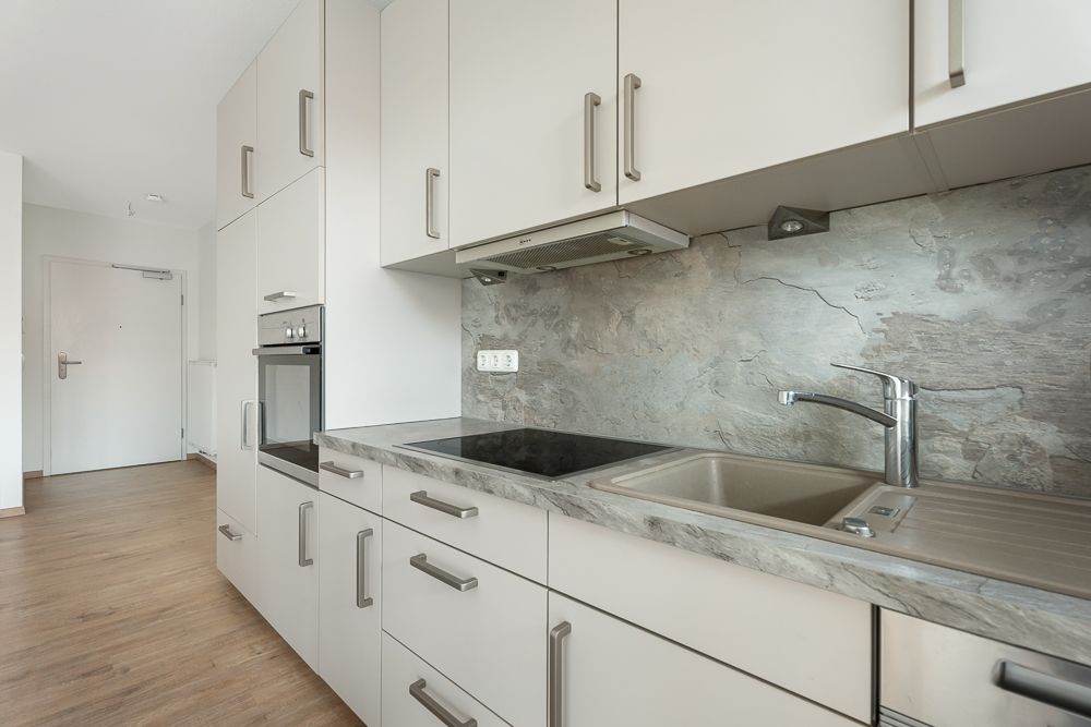 Moderne Einbauküche mit Herd, Spüle und weißen Schränken auf Holzfußboden.