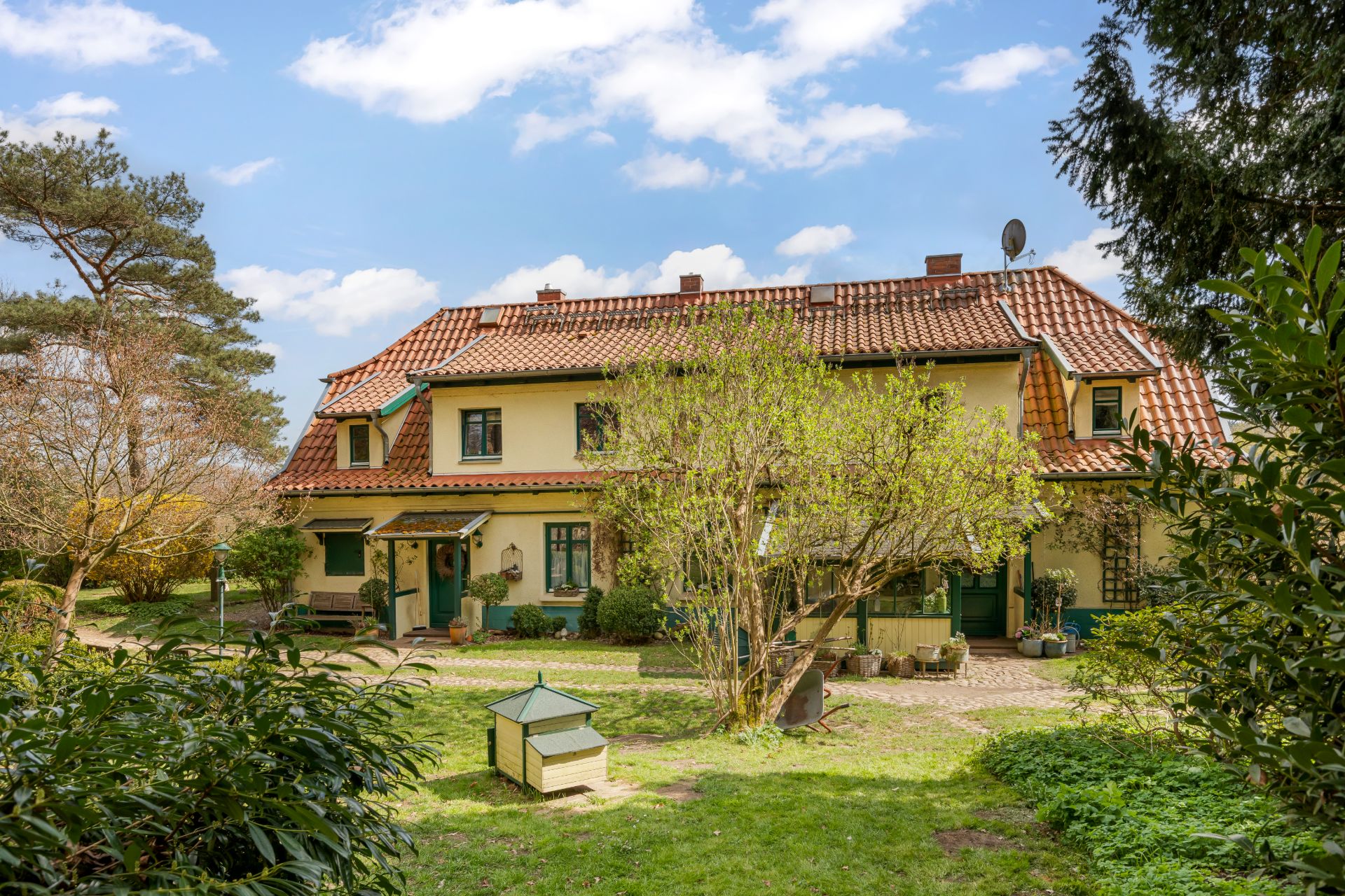 Zweistöckiges Wohnhaus mit rotem Ziegeldach, umgeben von Garten und Bäumen.