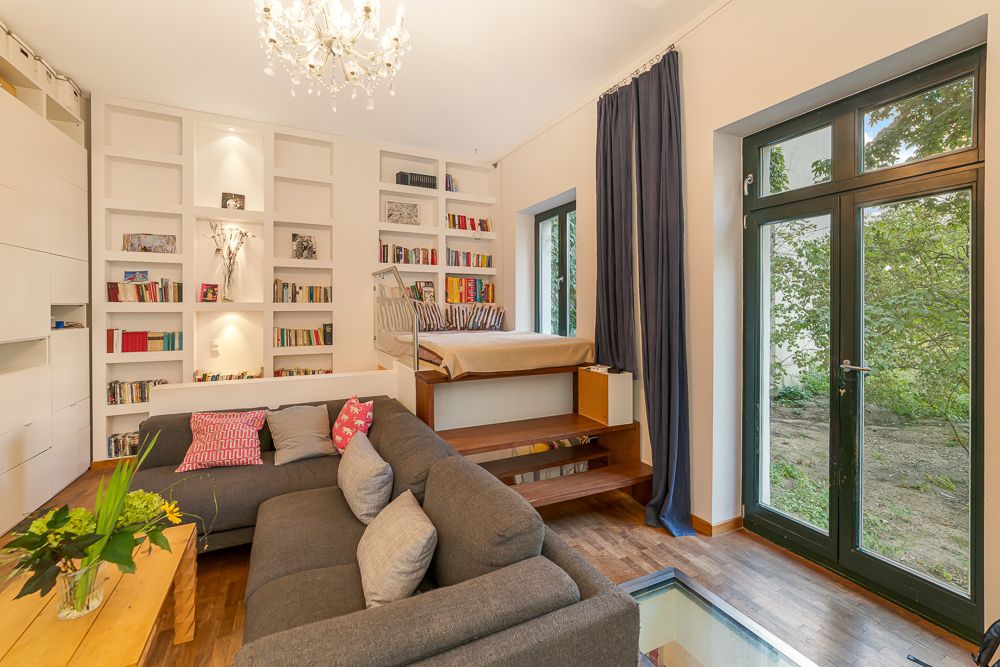 Helles Wohnzimmer mit Sofa, Bücherregal, Hochbett, Holzboden und großer Glastür zum Garten.