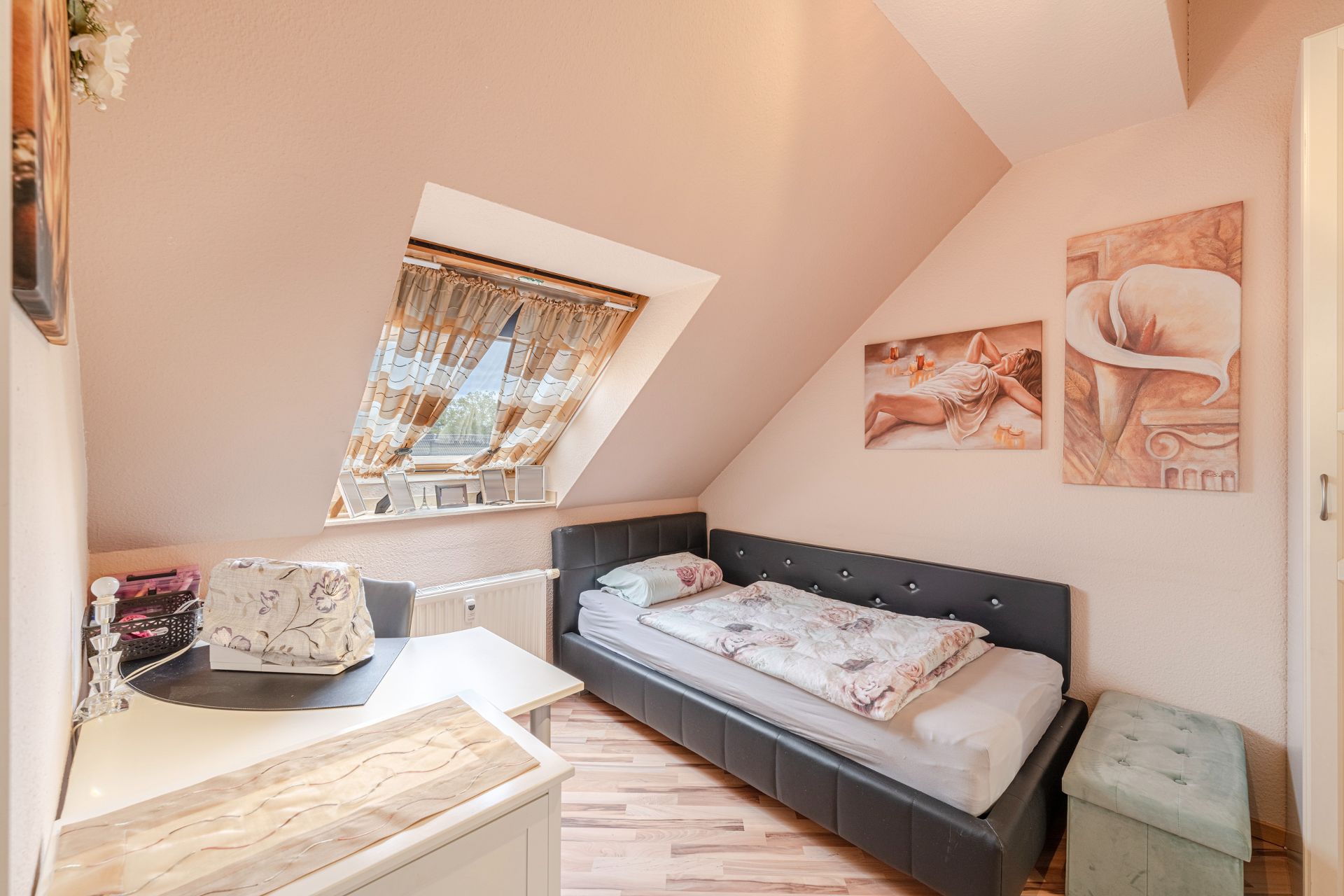 Kleines Schlafzimmer mit Einzelbett, Schreibtisch und Dachfenster mit Vorhang.