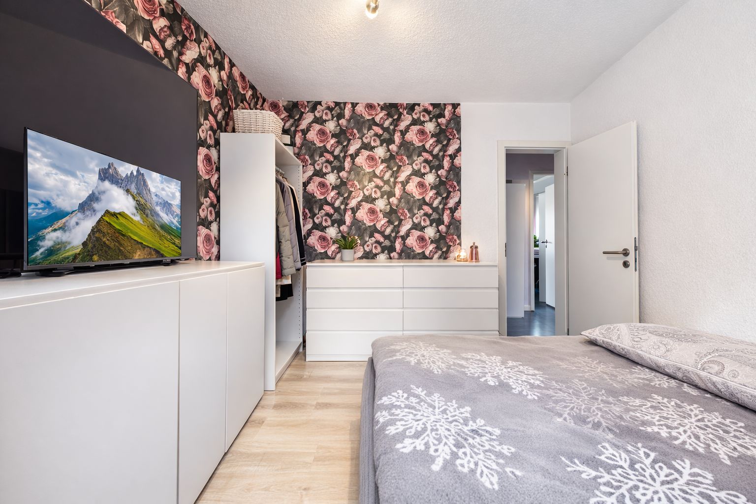 Modernes Schlafzimmer mit floral gemusterter Wand, Kleiderschrank, Kommode und Fernseher.