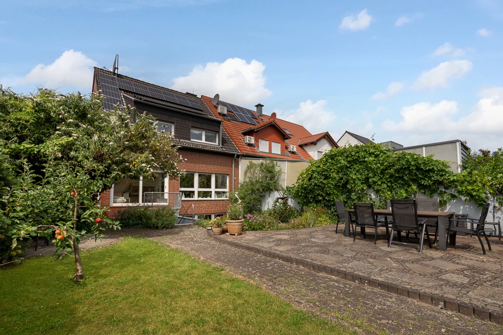 Garten mit Terrasse, Gartenmöbeln und angrenzendem Haus mit Solarpanels auf dem Dach.