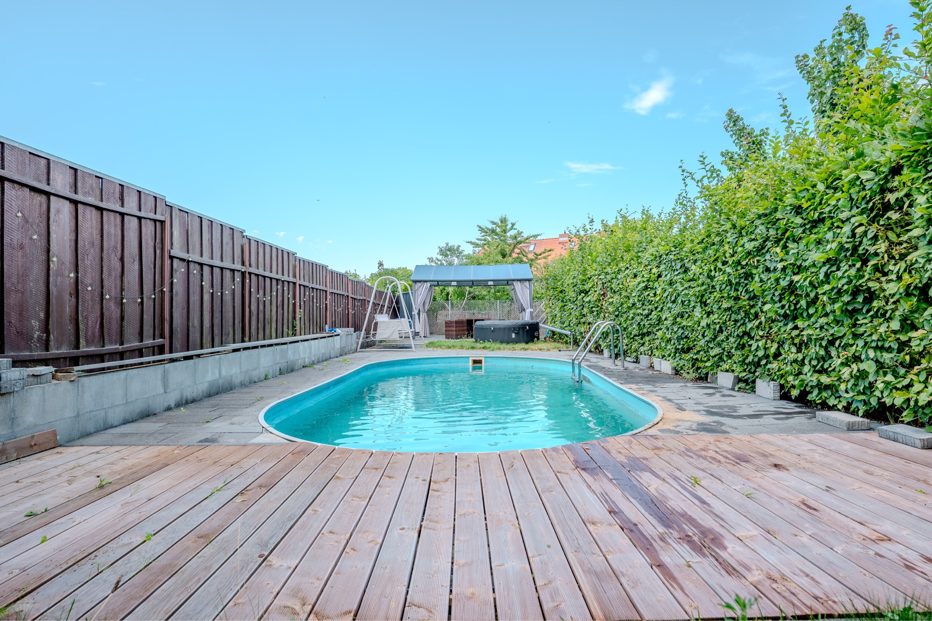 Swimmingpool im Garten mit Holzterrasse, Holzzaun und grüner Hecke.