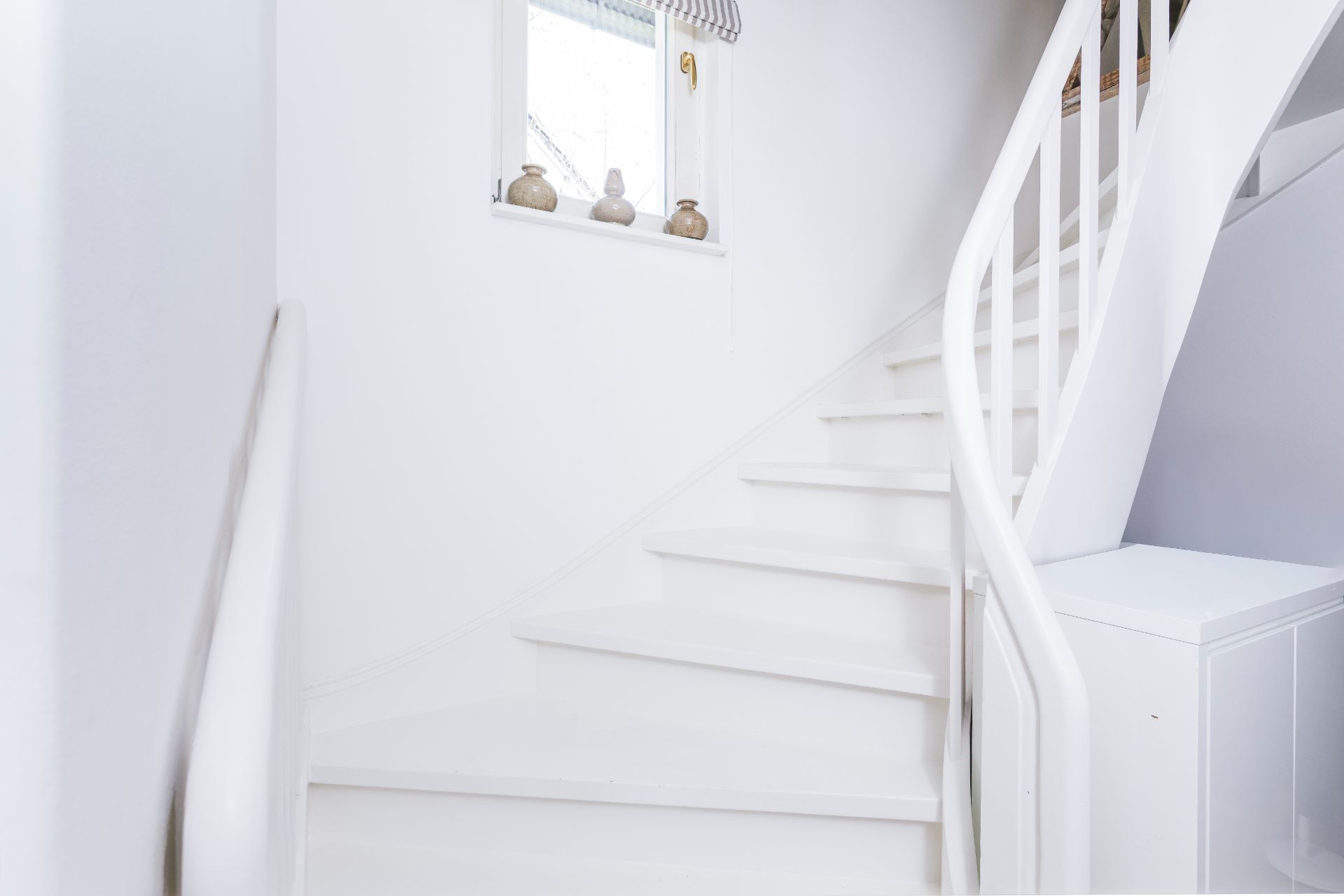 Weiße Treppe mit Fenster und dekorativen Vasen auf der Fensterbank.