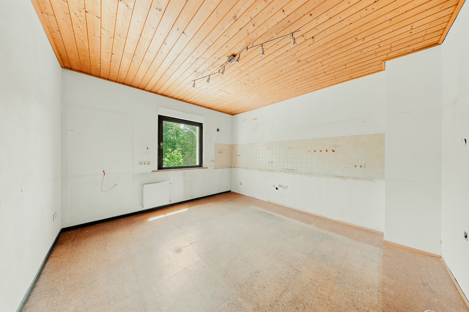 Leerer Raum mit Holzdecke, Fenster und Fliesen an einer Wand.