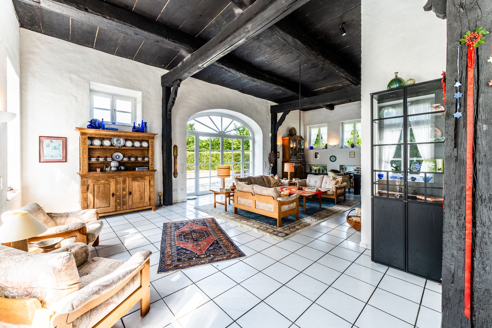 Helles Wohnzimmer mit weißen Fliesen, Holzmöbeln und großen Fenstern.