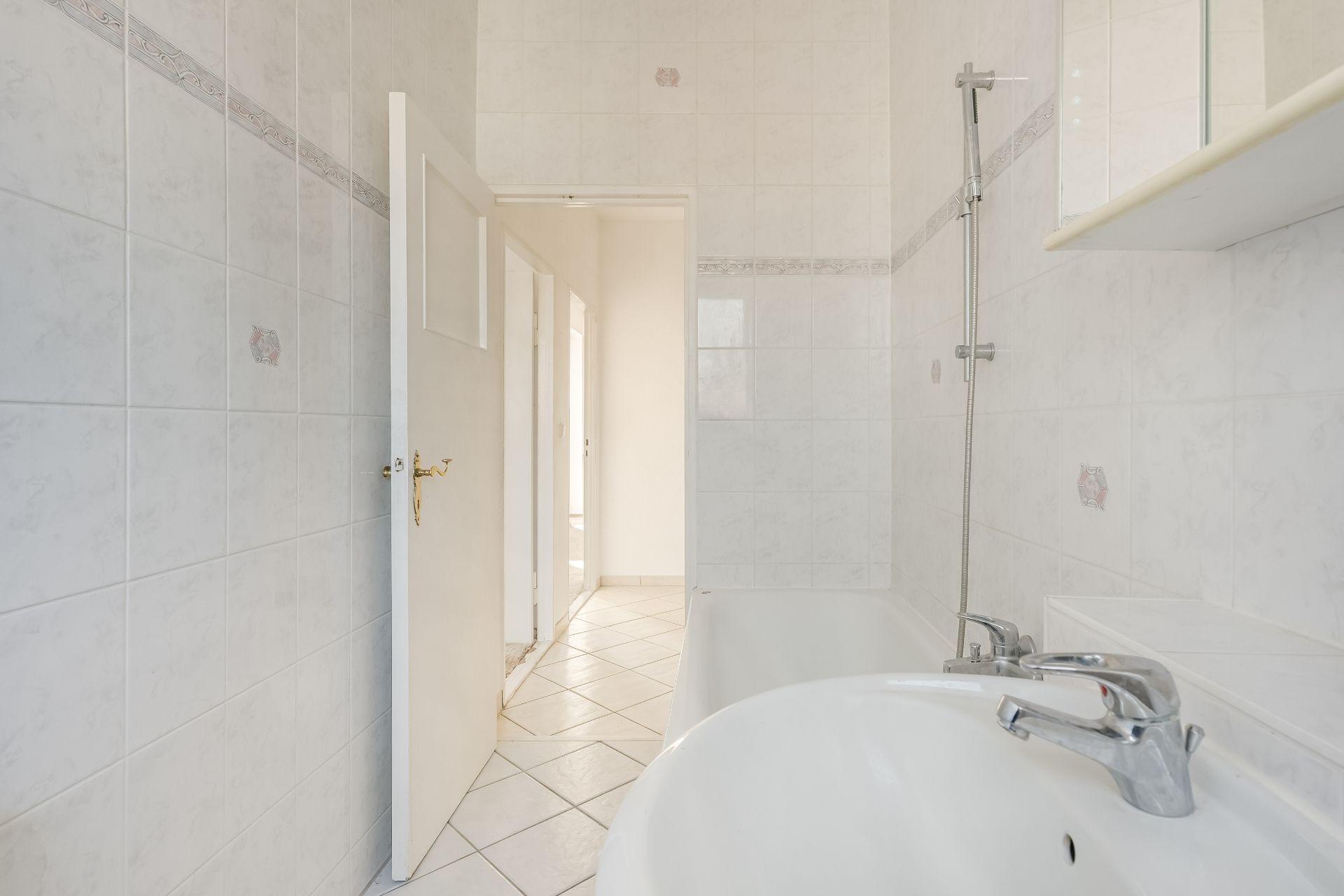 Helles Badezimmer mit Badewanne, Waschbecken und weißen Fliesen an Wand und Boden.
